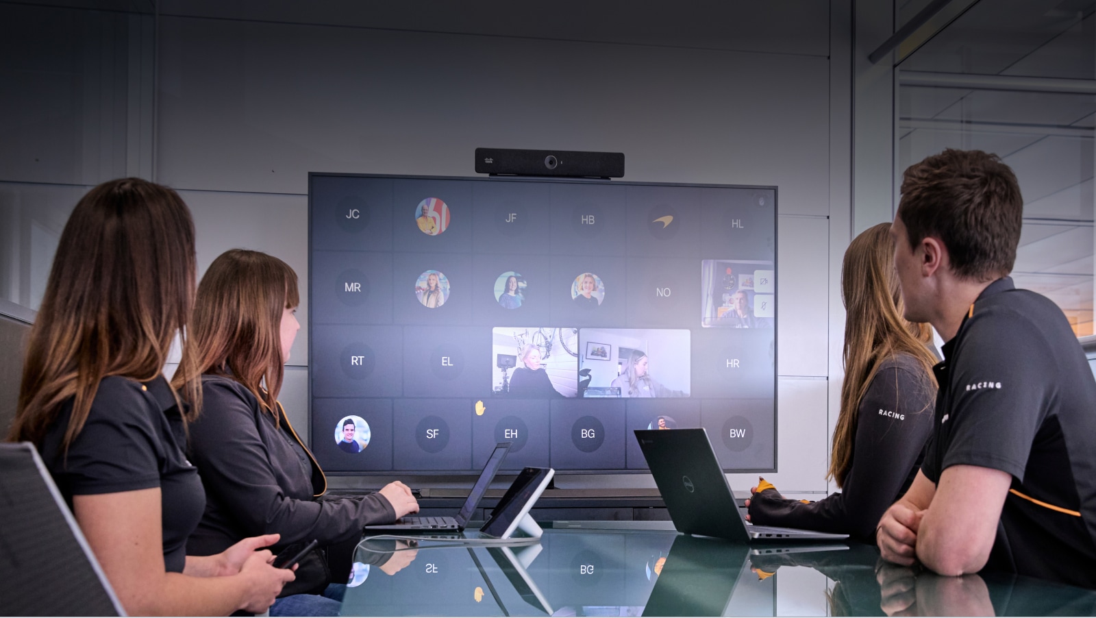 McLaren F1 Team members huddle in a conference room, connecting with others on a computer screen leveraging Cisco Webex collaboration solution.