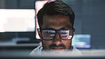 Man in black-framed glasses, with code reflected in his lenses